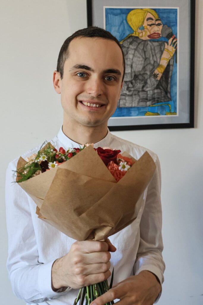 Maciej trzyma bukiet kwiatów na wernisażu